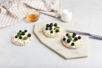 Crispbreads with cottage cheese and blueberries on light background