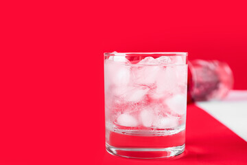 Glass of water with ice cubes on color background