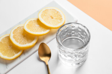 Glass of water and lemon on color background