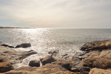 A low sun creating a glittering light over calm water  and rocks and stones in the foreground in the archepilago on the Swedish west coast