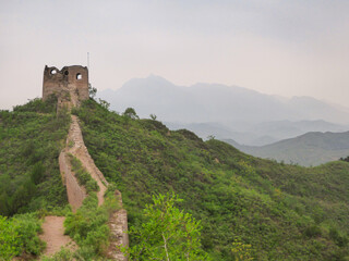 A panoramic view on an unrenewed Gubeikou part of Great Wall of China. The wall is spreading on tops of mountains. Many watchtowers on the peaks. Dense forest around it. World wonder. Tradition