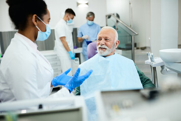 Happy senior man talking to dentist during appointment at dental clinic.