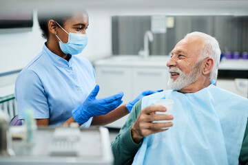 Happy senior man and dentist assistant talking during appointment at dental clinic.