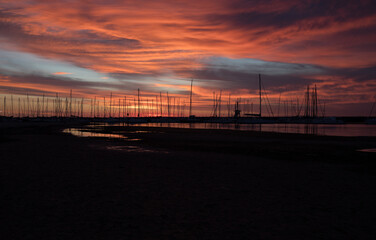 Silhouetted sailboats on orange color seascape over sunset sky.	