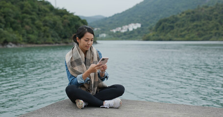 Woman sit on the pier and use of smart phone