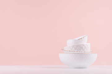 White porcelain bowls pile with thin gold border, different texture in soft light white, pastel pink kitchen interior. Fashion elegant minimalist design.