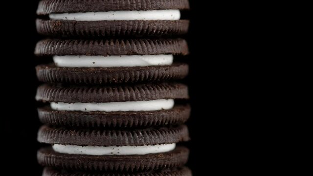 chocolate cookies with white cream close up on black background. the frame moves from bottom to top