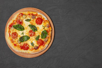 Pizza on wooden plate on black stone background. Cheese pizza with tomato, mozzarella and basil. Close-up photo. Copy space. 