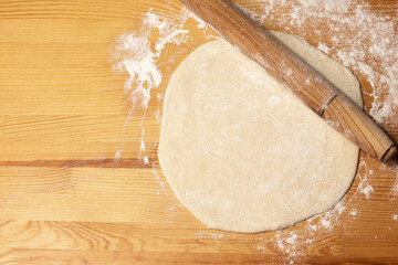Pizza dough on wooden background. Rolling-pin and flour. Selective focus, top view.
