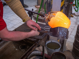 Artisan hands forming the red malleable glass on glassblower pipe.