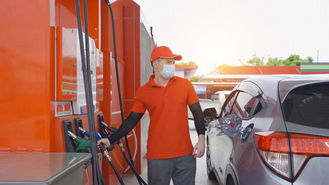 A Caucasian man, people, worker filling up fuel by using petrol pump at gasoline petrol station, wearing a face mask. refuel petroleum oil and energy vehicle business service. Coronavirus pandemic.