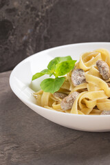 Close up of Tagliatelle noodles with mushrooms in cream sauce on white plate ready to eat. Mediterranean cuisine. Vertical orientation.