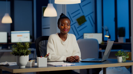 Portrait of business black woman looking at camera smiling raising head from laptop working in...