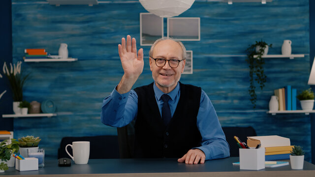 POV Of Elderly Aged Man Waving During A Video Conference With Business Partners Working From Home. Senior Person Using Internet Online Chat Technology Webcam Making Virtual Meeting Call Connection