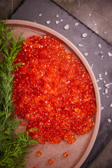 Delicious red caviar in a plate on the table, top view, dark background. A beautiful and rich dinner with red caviar. seafood and seafood delicacies