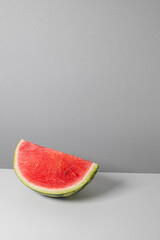 Creative art composition of a piece of ripe watermelon lies on the edge of the table. Minimalism trend concept. Vertical photo orientation