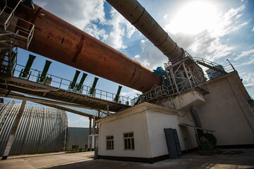 Standard Cement plant. Rotary clinker kiln, industrial building and tubes. Blue sky background.