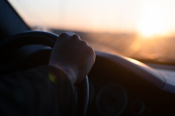 Men's hands hold the steering wheel in the car on a trip at sunset. Journey. Blur.