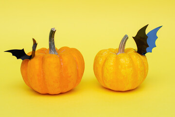 Orange Halloween pumpkins with carved black decorative bats on them, on a yellow background.