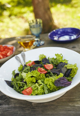 Fresh salad mix of arugula leaves, basil, lambs lettuce and tomatoes. Salad bowl, healthy food. Composition in a white plate on an old wooden table