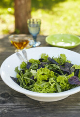 Fresh salad mix of arugula leaves, basil, and lambs lettuce. Salad bowl, healthy food. Composition in a white plate on an old wooden table