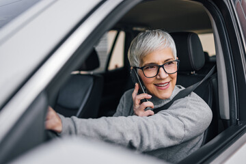 Close-up portrait of an older woman driving a car and talking on smart phone.