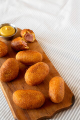 Homemade Mini Corn Dogs on a rustic wooden board on cloth, side view. Copy space.
