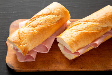 Homemade Parisian Jambon-Beurre Sandwich on a rustic wooden board on a black background, side view....