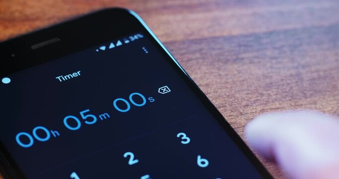 Person sets five minutes in timer app on contemporary mobile phone with black display by finger on table extreme close view
