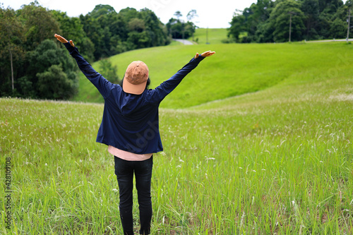 A woman raises her hands and gets fresh air after the rain in the green meadow of the national park.