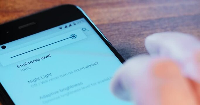 Person Changes Screen Brightness Level In Settings Of Contemporary Smartphone By Finger On Wooden Table Extreme Close View