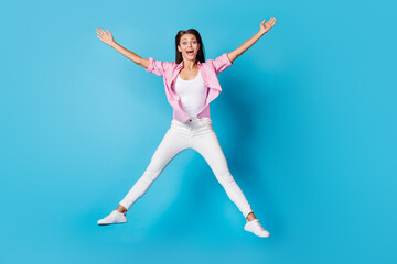 Fototapeta na wymiar Photo of lady jump raise hands star pose open mouth wear pink striped shirt trousers sneakers isolated blue background
