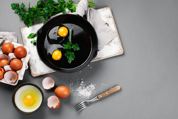 Raw eggs in pan with herbs and seasoning on gray background, prepared food for breakfast.