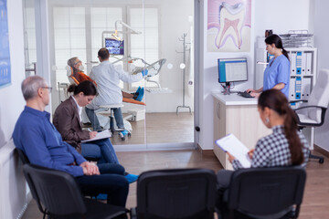 Dentist doctor treating senior woman teeth in stomatology clinic. Patient in waiting area filling...