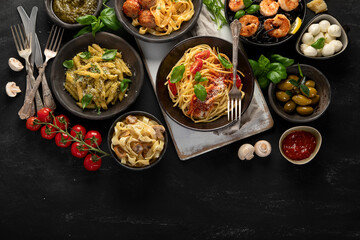 Assortment of Italian pasta with traditional sauces for dinner on dark background.