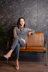 young woman sits on a leather armchair in formal clothes, a variant of an office wardrobe.