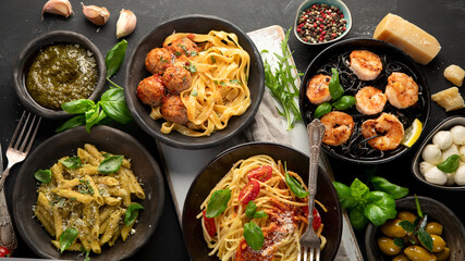 Assortment of Italian pasta with traditional sauces for dinner on dark background.
