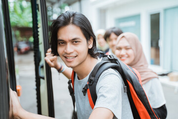close up of an Asian man wearing a backpack holding a door handle getting into the bus with the background of passengers lining up