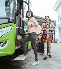 asian woman with headphones and bag smiling to the camera when stepped into the bus for go to...