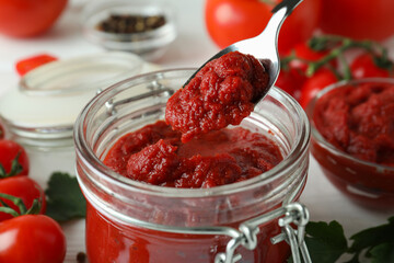 Jar and spoon with tomato paste on white wooden table with ingredients