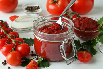 Jar and spoon with tomato paste on white wooden table with ingredients