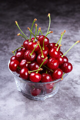 Fototapeta na wymiar Close-up of wet cherries in glass bowl on grey background