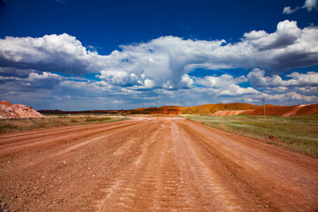 Fototapeta na wymiar Colorful landscape of bauxite mine (aluminium ore quarry). Orange soil and road and blue sky with clouds.