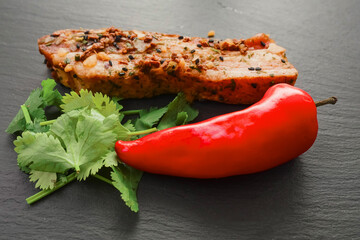 Raw Asian style marinated pork belly slice with red pepper and coriander on black stone board. Meat with herbs and spices. Meat industry product.