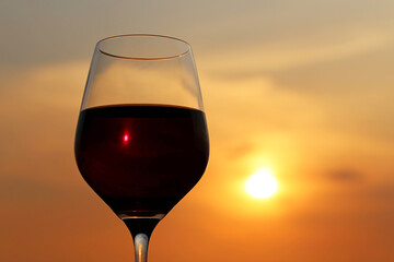 Glass with red wine on sunset background, evening sun is shining through the glass. Concept of celebration, wine industry