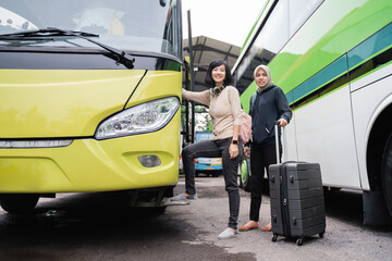 Fototapeta na wymiar a short-haired woman with headphones and a bag smiling at the camera as she steps up to the bus door with a woman in a headscarf carrying a suitcase behind her while going by bus