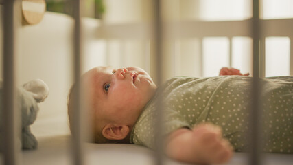 Authentic Close Up Shot of a Cute Newborn Baby Lying on the Back in Child Crib. Playful Portrait of a Caucasian Neonate Toddler at Cozy Home Space. Concept of Childhood, New Llife and Parenthood.