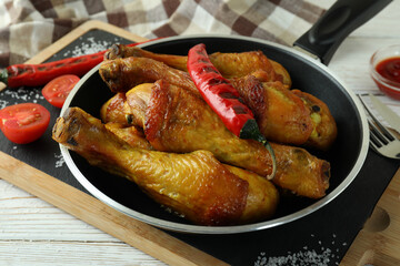Concept of delicious eating with pan of roast chicken drumsticks on white wooden table