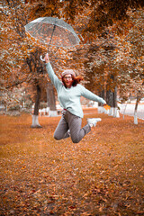 Cheerful Caucasian girl jumping up with a transparent umbrella in the autumn park. Happiness and fun in the rain