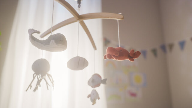 Rotating Wooden Crib Toy with Stuffed Animals Hanging Above Newborn Baby Bed. Cozy, Sunny and Authentic Child's Bedroom with Colorful Drawings on Walls. Concept of Childhood, New Llife and Parenthood.